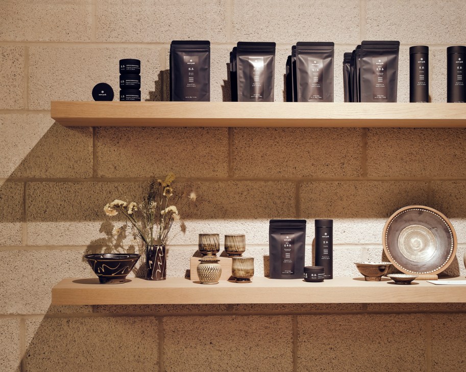 Wooden shelves displaying dark tea packages and ceramic bowls with dried flowers in vase
