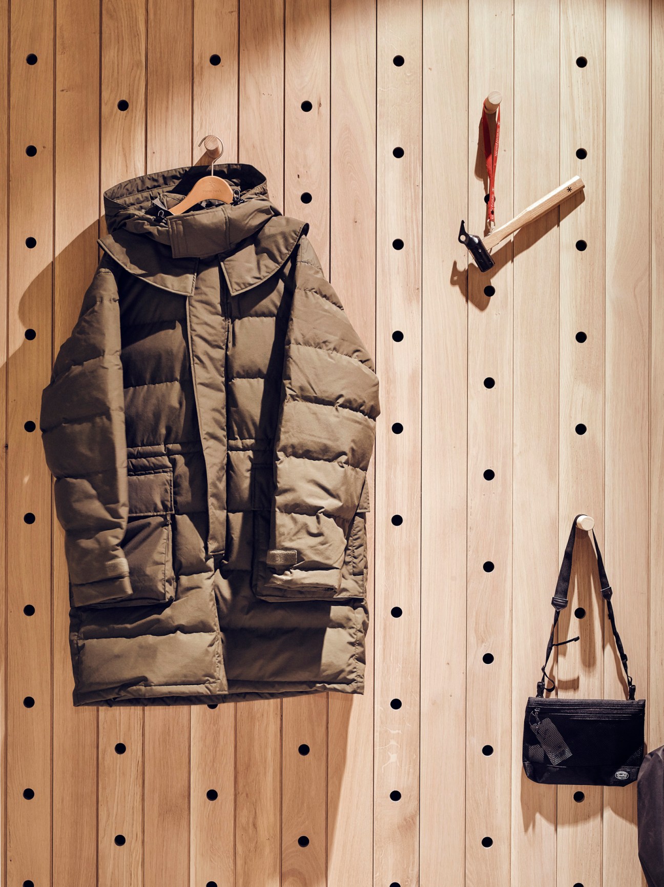 Snow Peak FR down coat hanging on wooden pegboard display with camping accessories