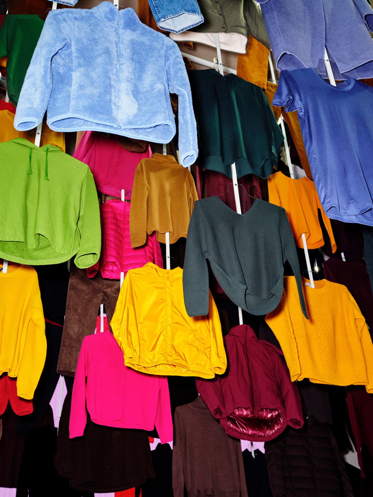 Colorful array of clothing items hanging on display including sweaters, jackets and garments in various bright colors
