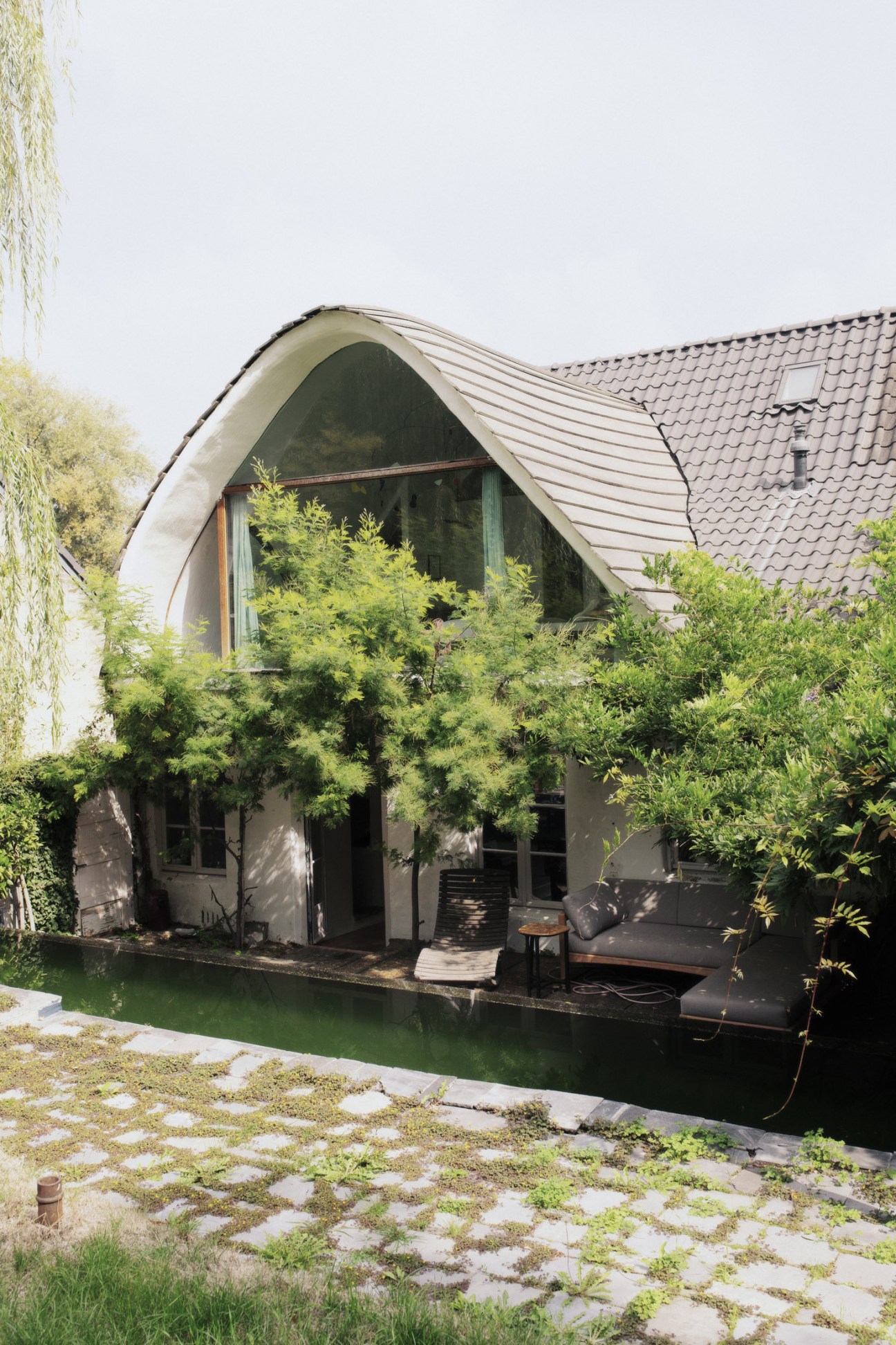 Curved wave-shaped window extension of Valentin Loellmann's renovated home in Maastricht overlooking a pool and garden.