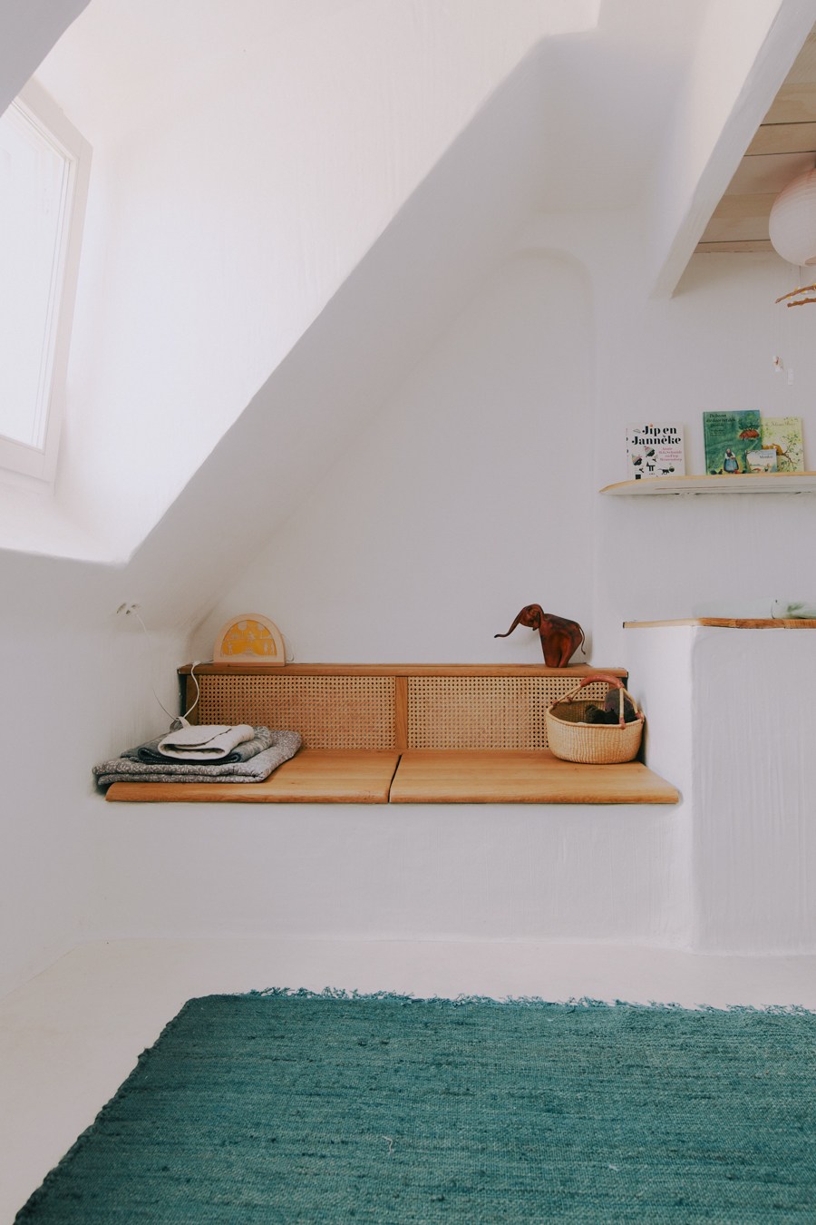 Children's bedroom with white walls, wooden shelf with rattan backing, books, toys and storage baskets.