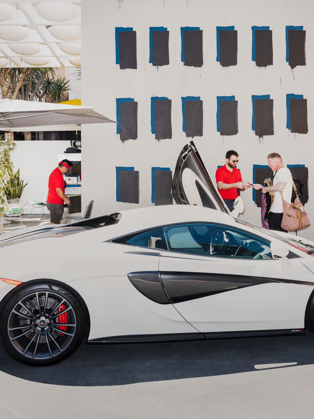 Valet attendant in red polo shirt handing keys to customer at luxury hotel with modern art wall.
