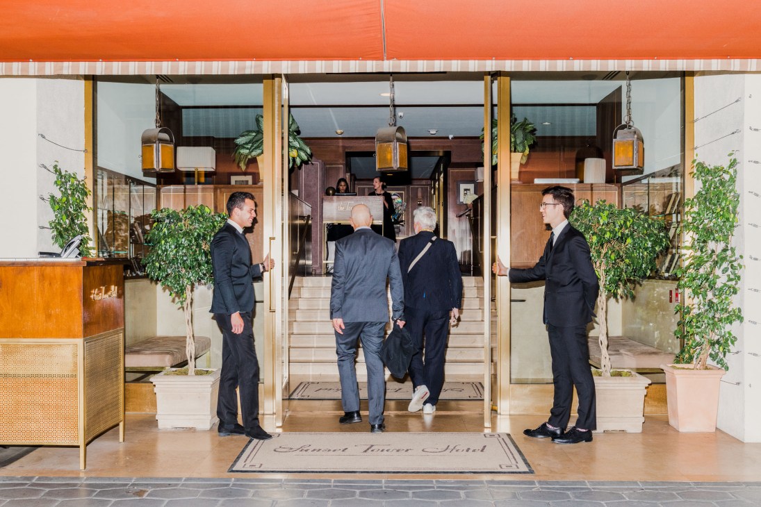 Valet attendants in dark suits stand at the entrance of the Sunset Tower Hotel, welcoming guests under an orange awning.