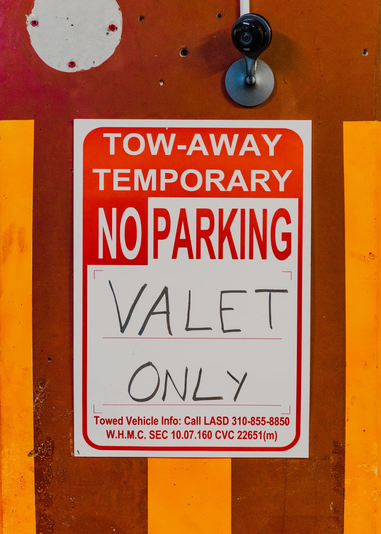 No parking sign with hand-written "VALET ONLY" text on orange and red striped wall
