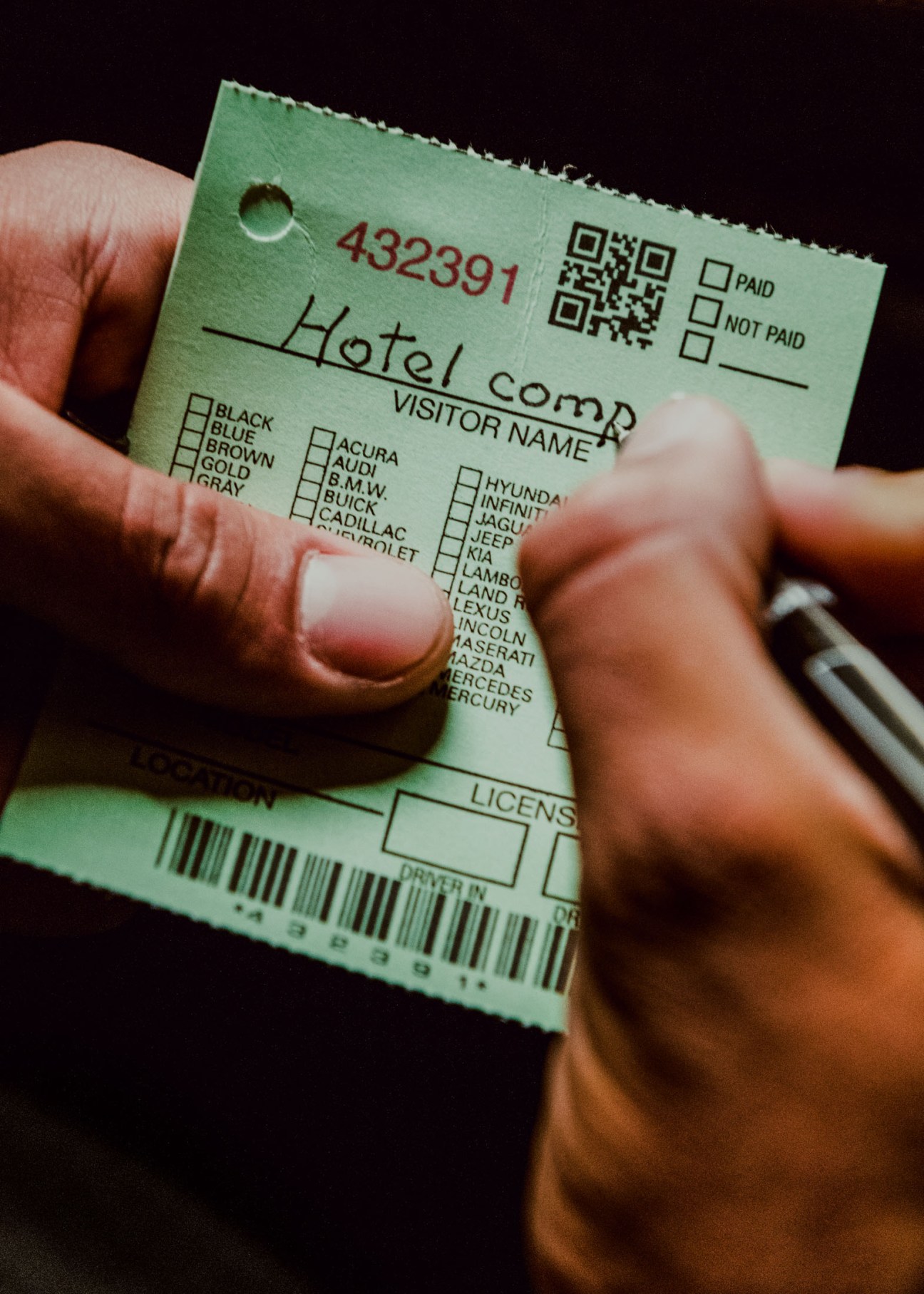 Hands holding a green valet parking ticket with vehicle checklist and QR code.