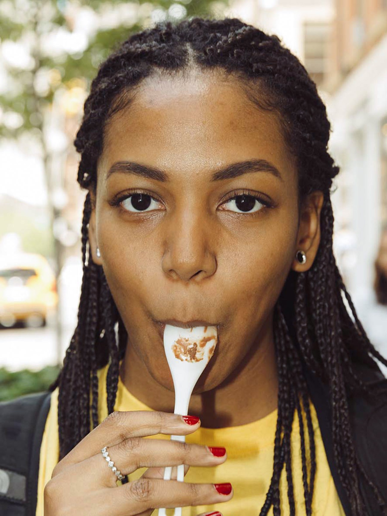 Woman in yellow shirt eating a popsicle with a white stick and brown topping.
