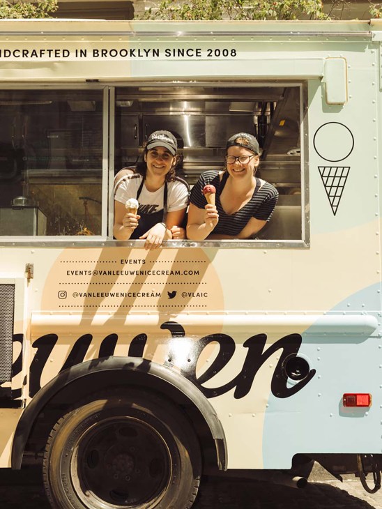 Two women holding ice cream cones at the window of a Van Leeuwen ice cream truck in Brooklyn.