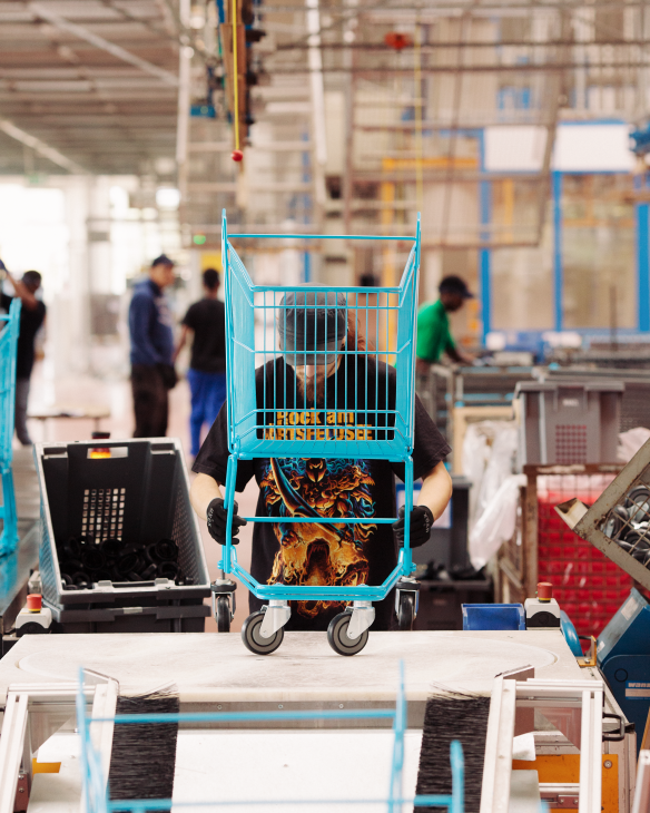Factory worker assembling wire components into a shopping trolley basket structure on the production line