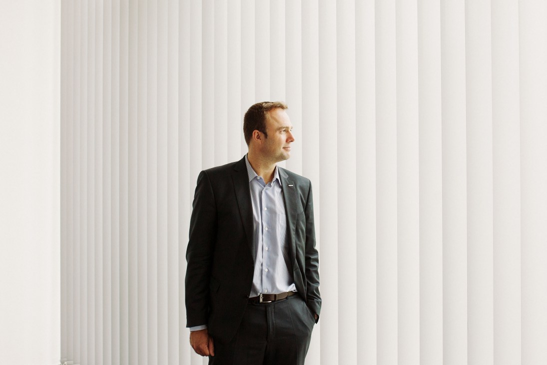 Andreas Starzmann, director of Wanzl's digital office, stands against a white vertical blinds background wearing a dark blazer and light blue shirt.