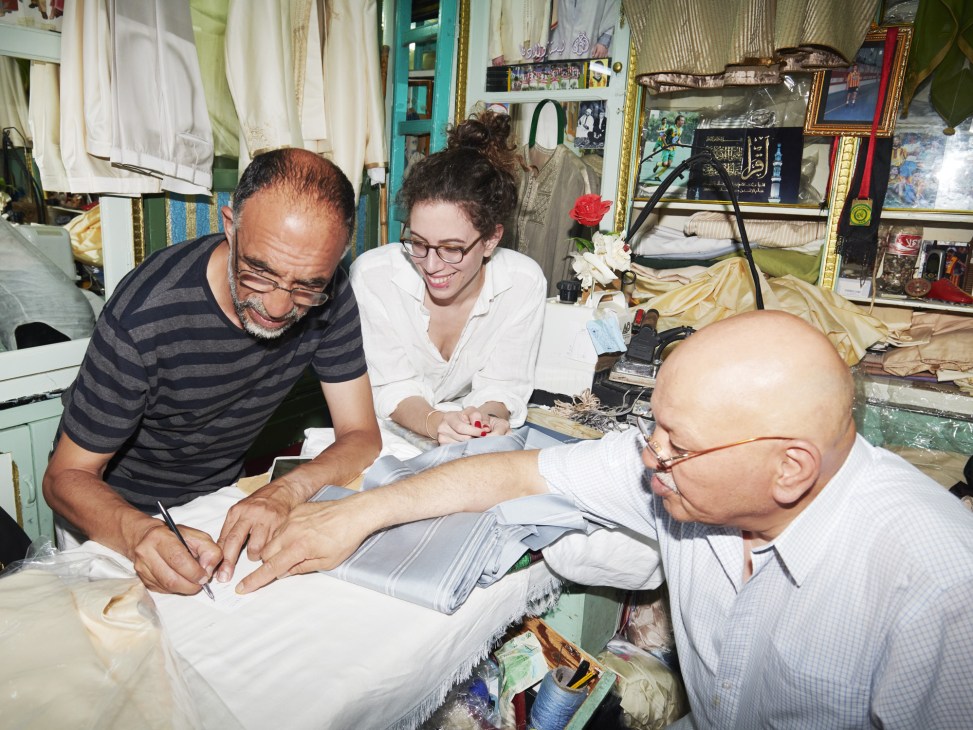Designer Deborah Neuberg meeting with two Tunisian embroiderers in their workshop space surrounded by textiles and craft materials.