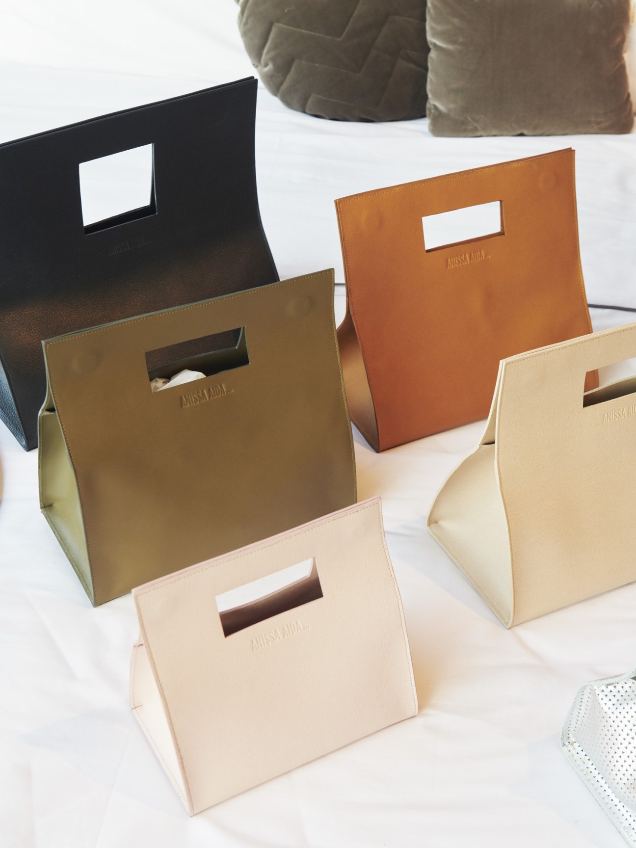 Anissa Aida handbags in various colors displayed on white surface
