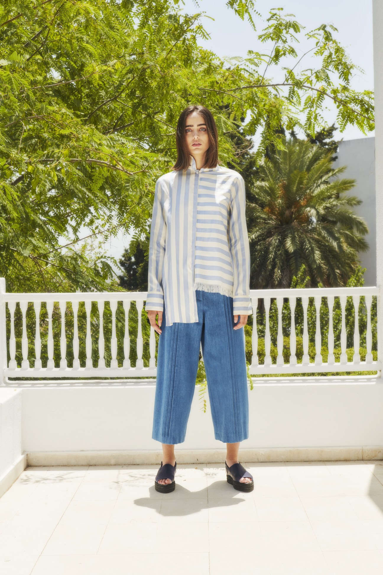 Model wearing Anissa Aida striped shirt and blue denim cropped pants in asymmetric design.