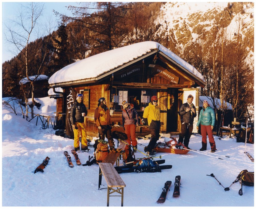 Skiers gather at a wooden mountain hut during golden hour at Les Rochers des Mottets in La Vallée Blanche.