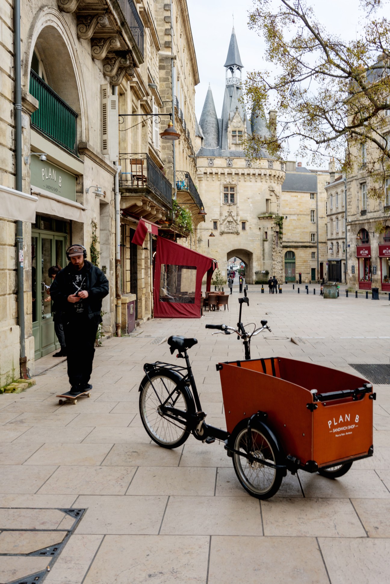 A cargo bike with an orange box delivering goods in a Bordeaux street with medieval architecture.