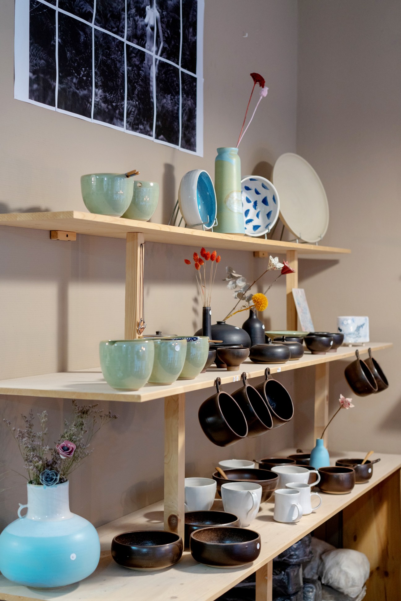 Wooden shelves displaying ceramic bowls, plates, black cookware, white mugs, and blue vases with dried flowers.
