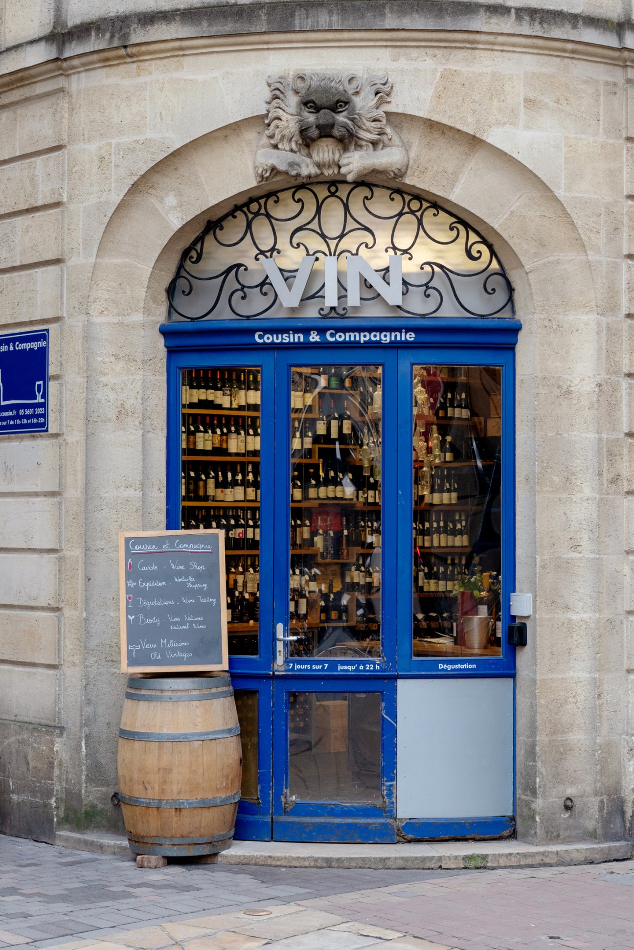 Blue storefront wine shop with ornate stone facade and wine barrel outside in Bordeaux city centre