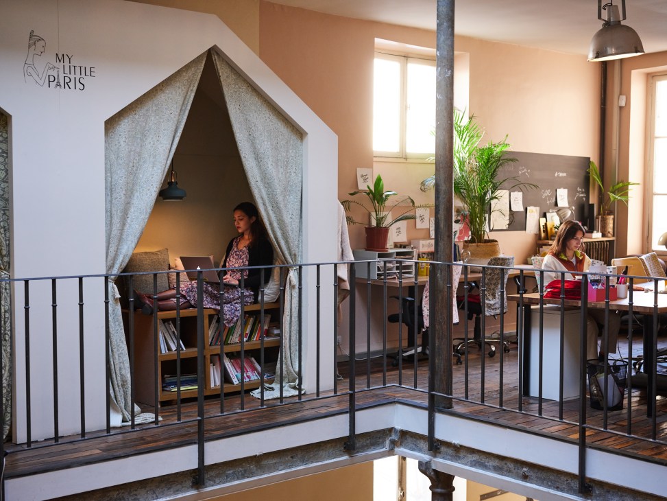 An employee works in a tent-like cosy corner at My Little Paris offices with bookshelves and plants.