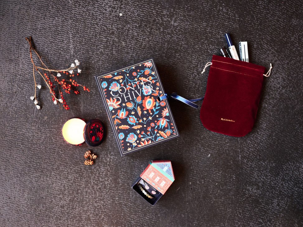 Contents of a My Little Box subscription service displayed on gray fabric, including a decorative box, cosmetics, velvet pouch, and botanical accents.