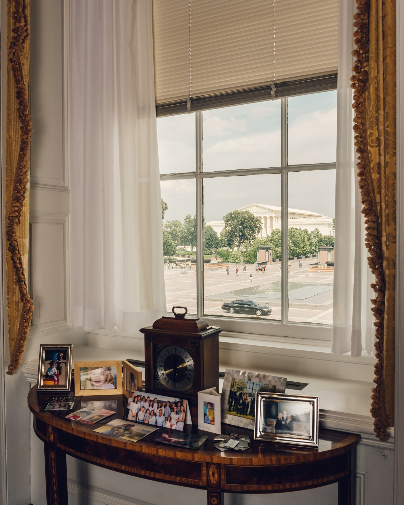 View from office window showing desk with family photos, clock, and government building in distance