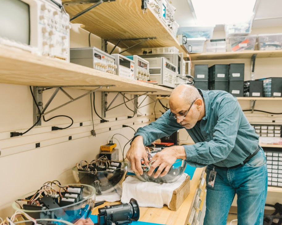 Engineer Mohsen Ahmed works on an underwater-camera casing at a workbench surrounded by electronic equipment.
