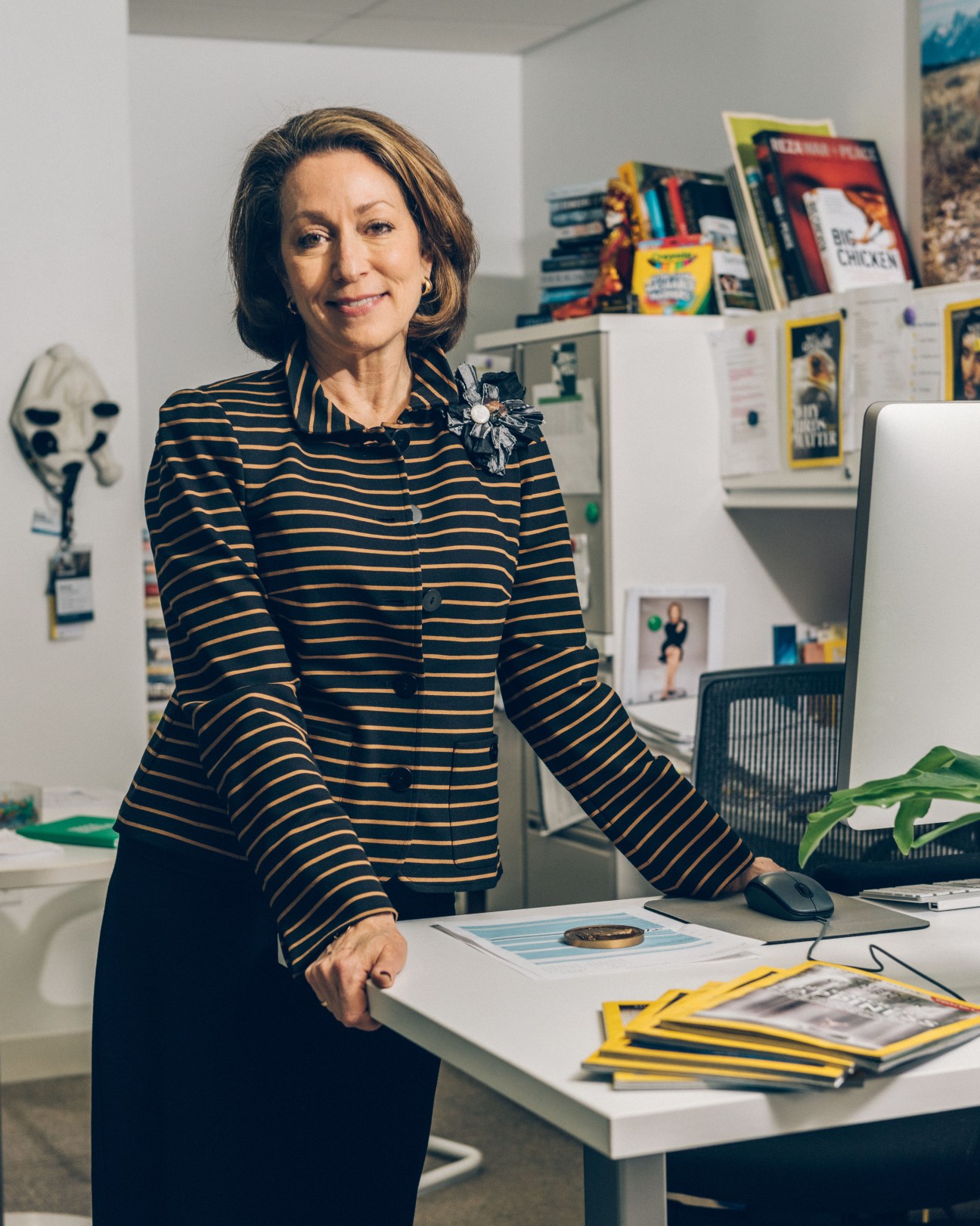 Susan Goldberg, editor in chief of National Geographic, stands at her desk with magazines displayed.