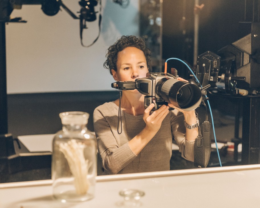Photographer Becky Hale holds a professional camera while shooting jars of wild fungi in a studio setting.