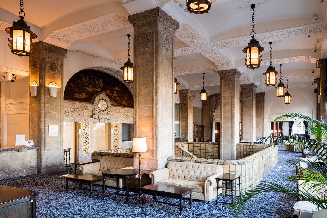 Hotel New Grand's lobby lounge with cream tufted sofas, mahogany pillars, ornate ceiling, and hanging lanterns.