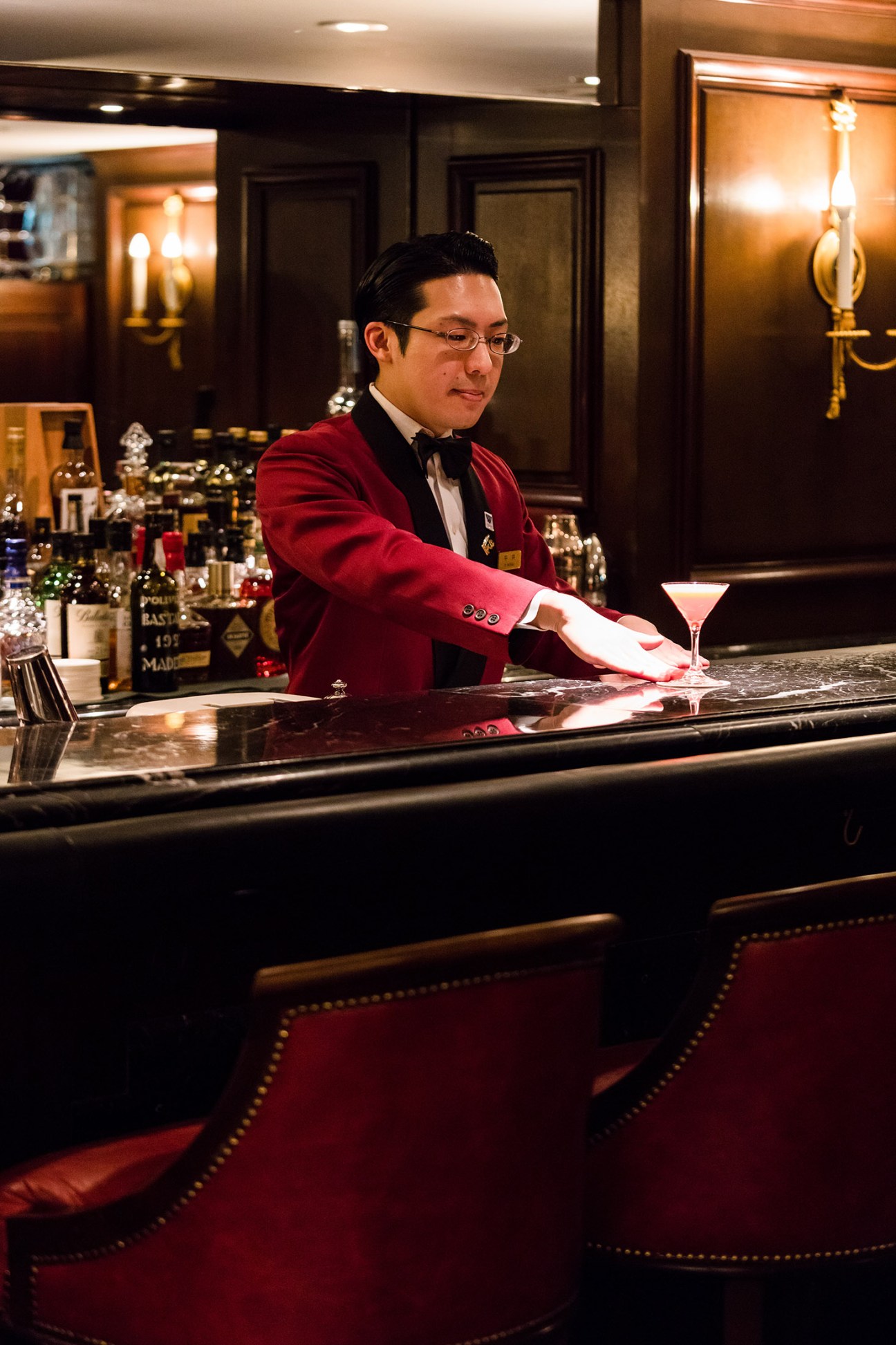 Bartender in red jacket and bow tie polishing glass at the Sea Guardian II bar counter.