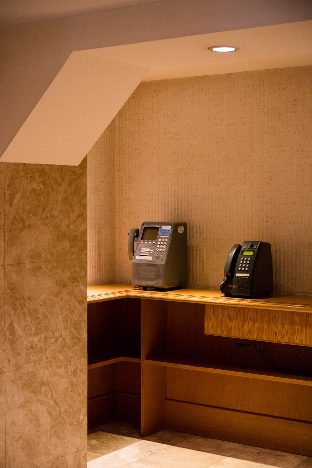 Two vintage payphones on a wooden counter in a warm-toned hotel alcove with textured walls.