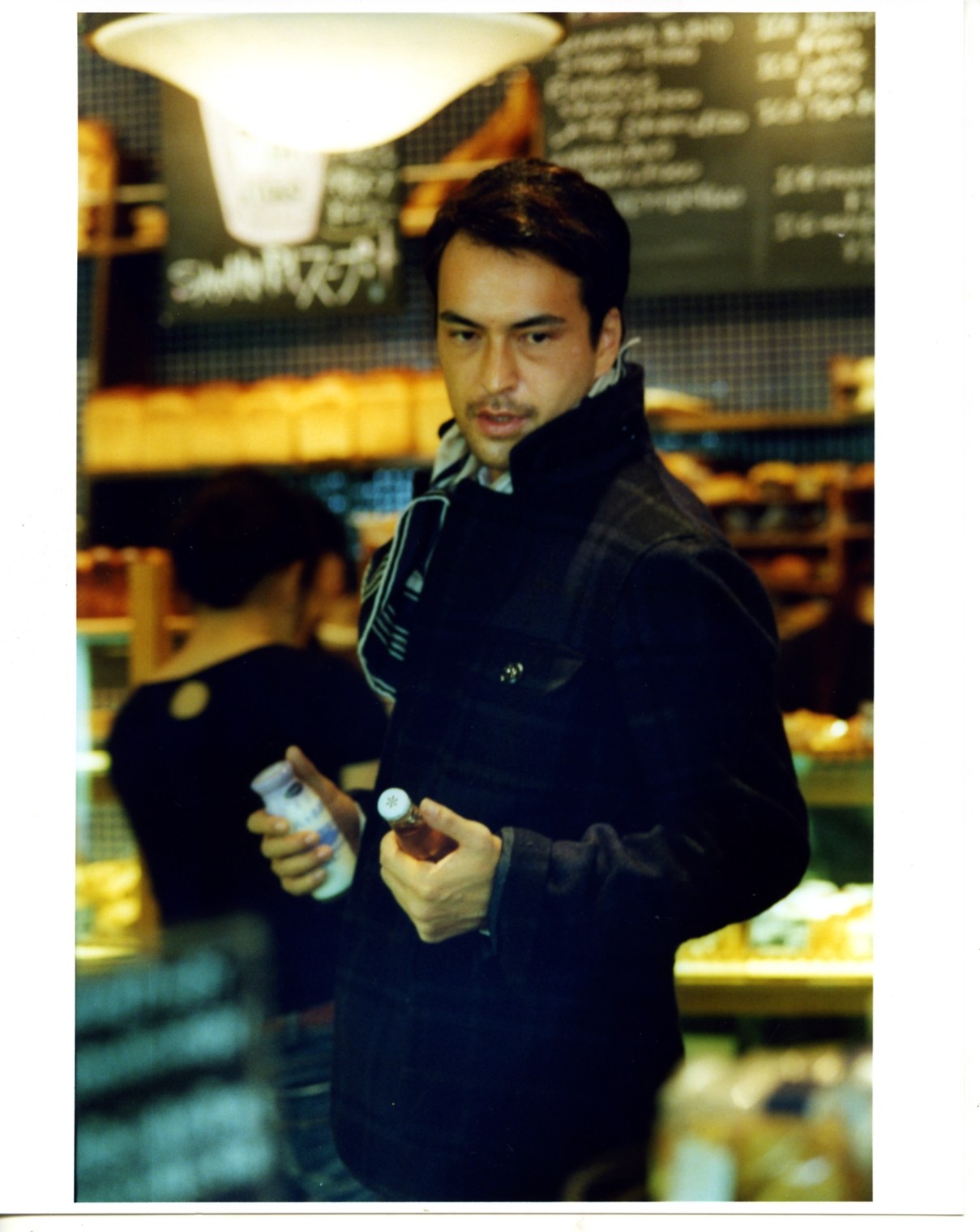 Man wearing Woolrich John Rich & Bros jacket and Hermès scarf in a café setting.