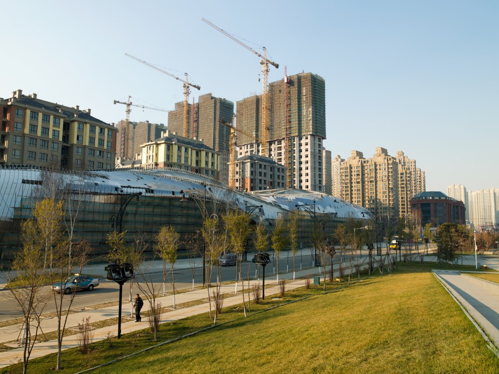 Harbin's Qunli New District under construction with modern high-rise apartment towers, construction cranes, and landscaped green spaces.