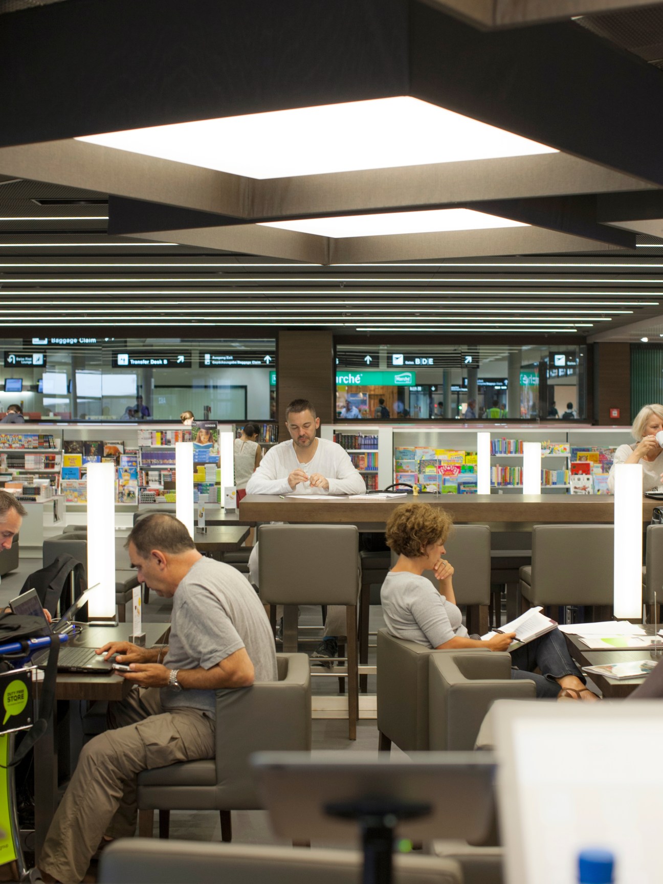 NZZ Café at Zürich airport with customers reading newspapers and magazines at modern seating areas.