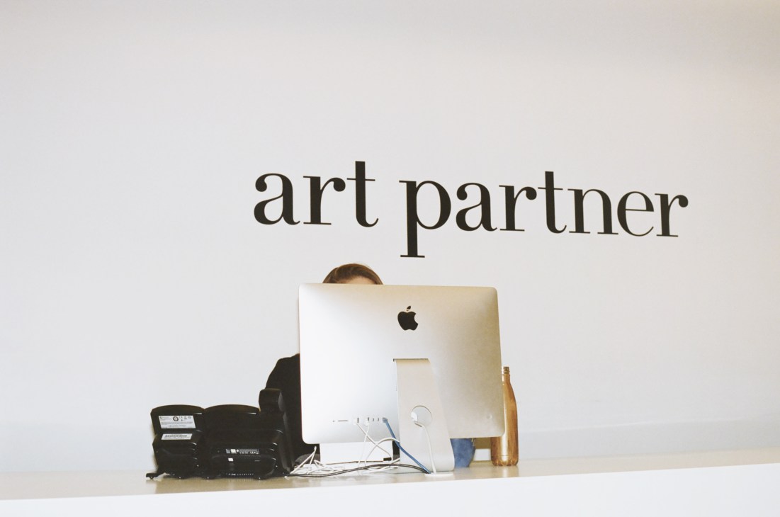 Art Partner office reception desk with person behind iMac computer and company name on wall