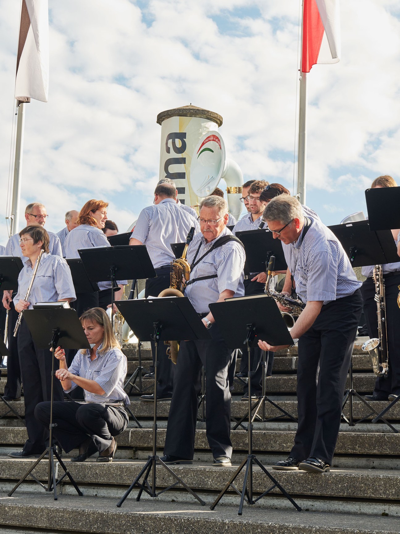 A brass band in blue striped shirts performs at an outdoor fair with Swiss flags and an Olma banner visible.