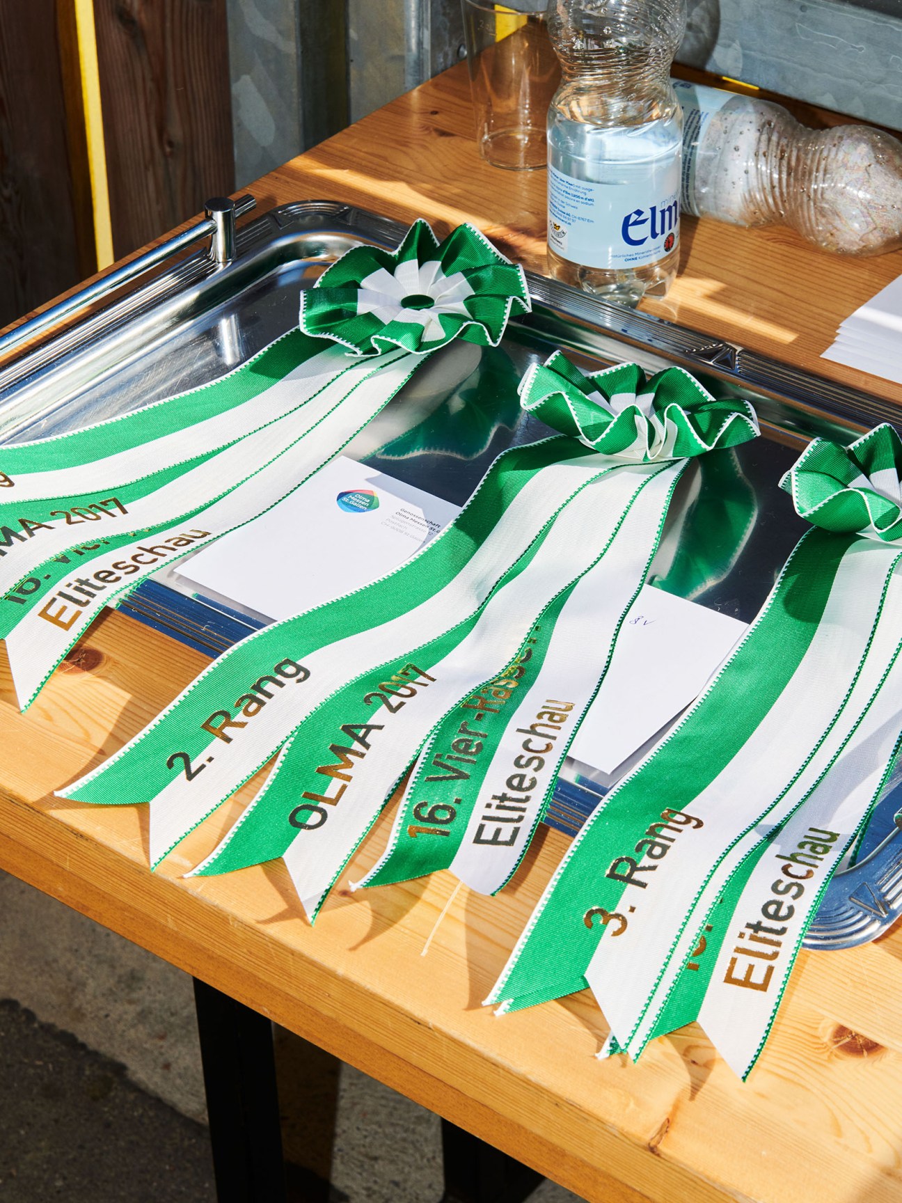 Green and white ribboned medal awards displayed on a wooden table with water bottles.