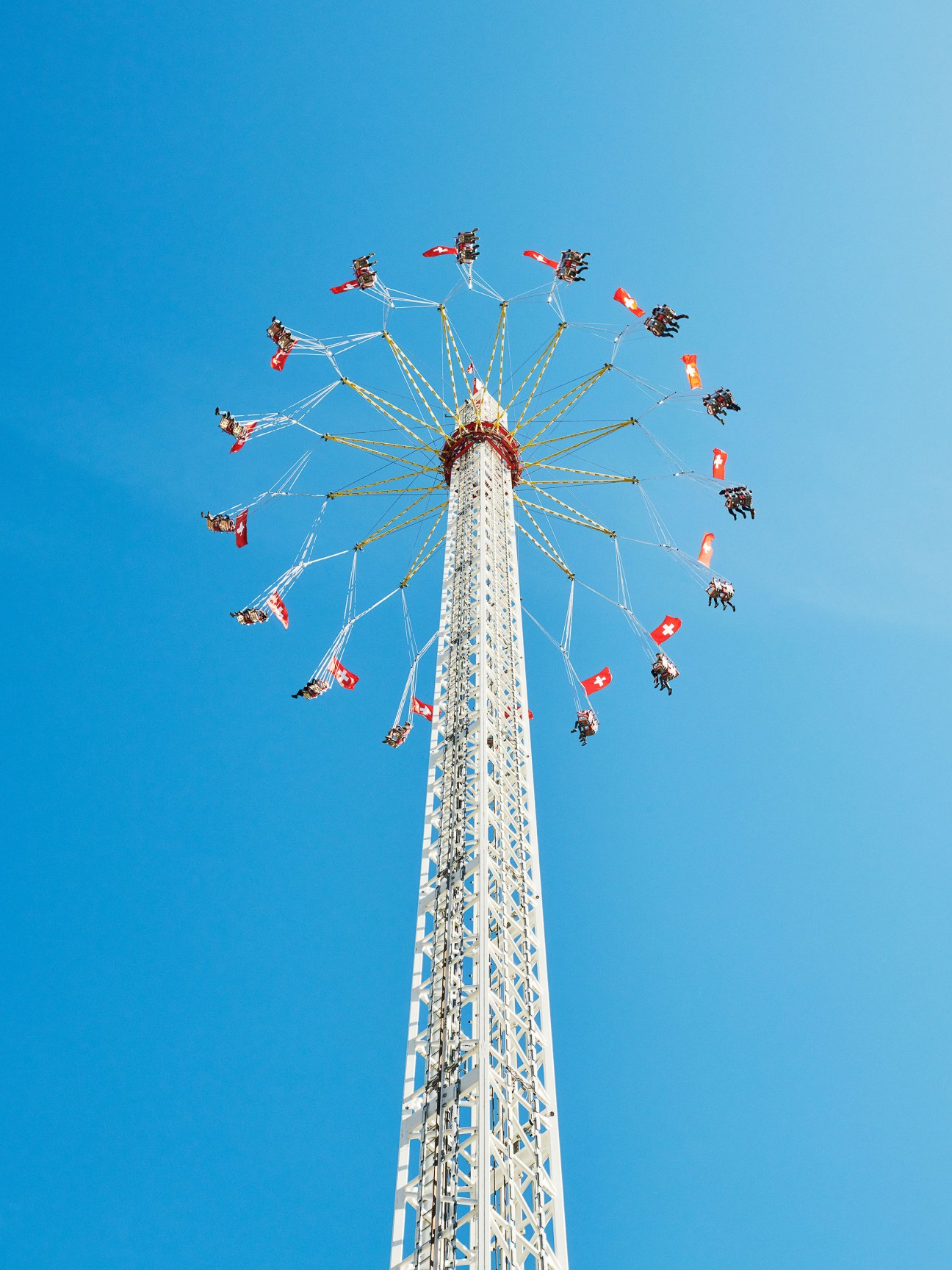 A chain swing ride at Olma fair with Swiss flags, photographed from below against clear blue sky.