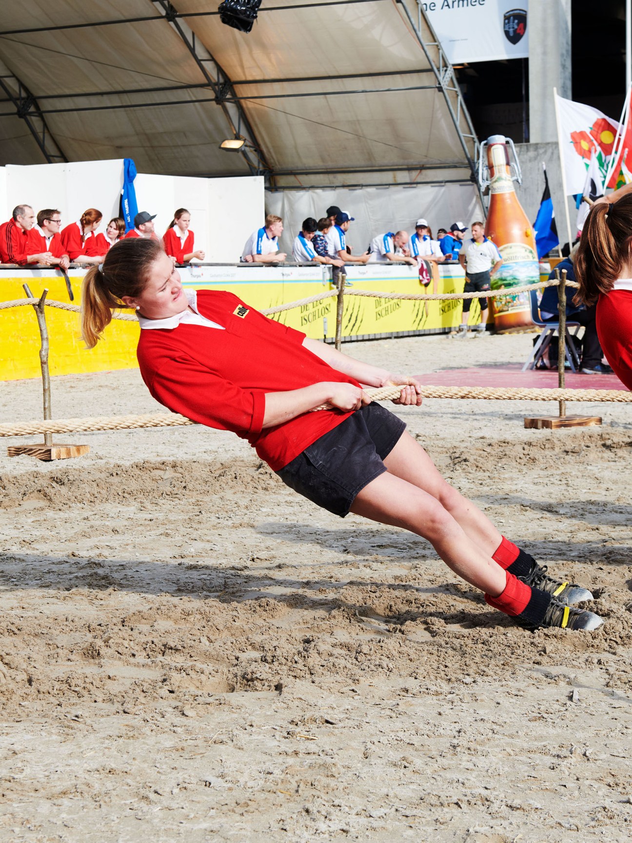 Woman in red shirt pulls rope during tug-of-war competition at Olma fair in sand arena.
