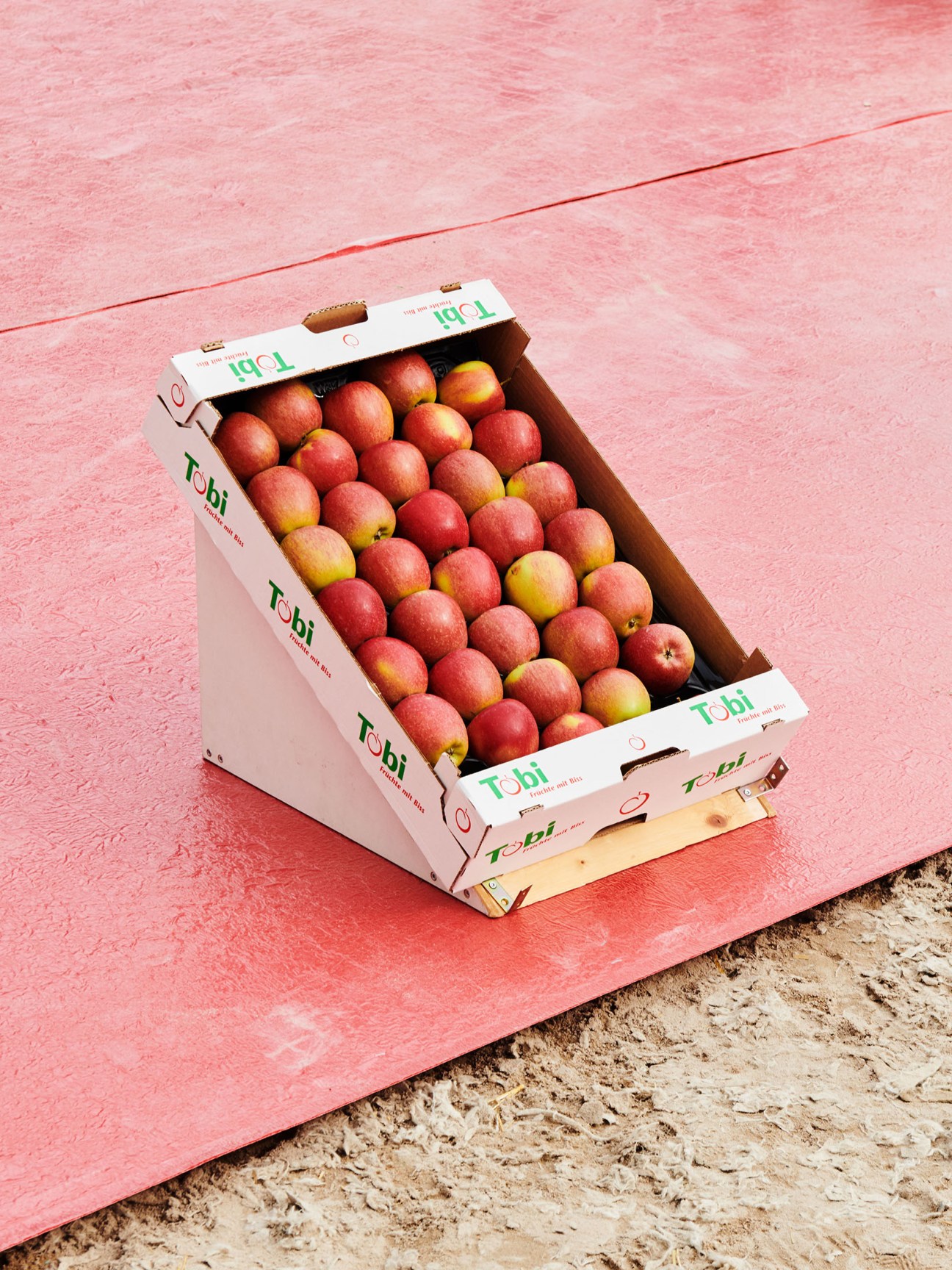 Box of red apples with Töbi branding on pink background