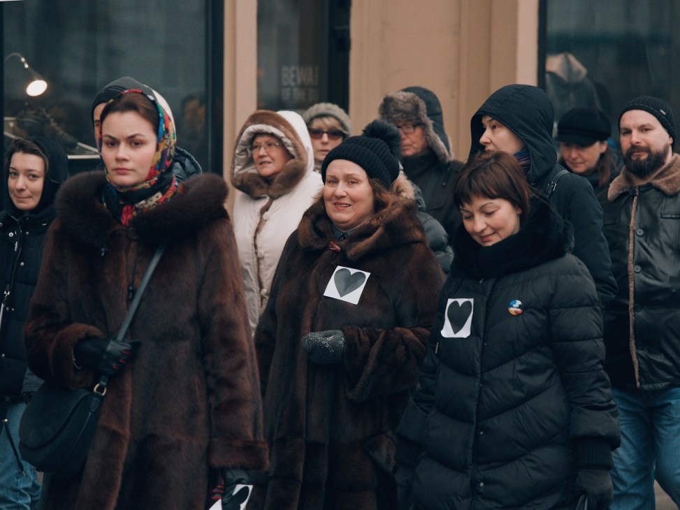 Russian protesters wearing black heart symbols stand together on a street during a demonstration.