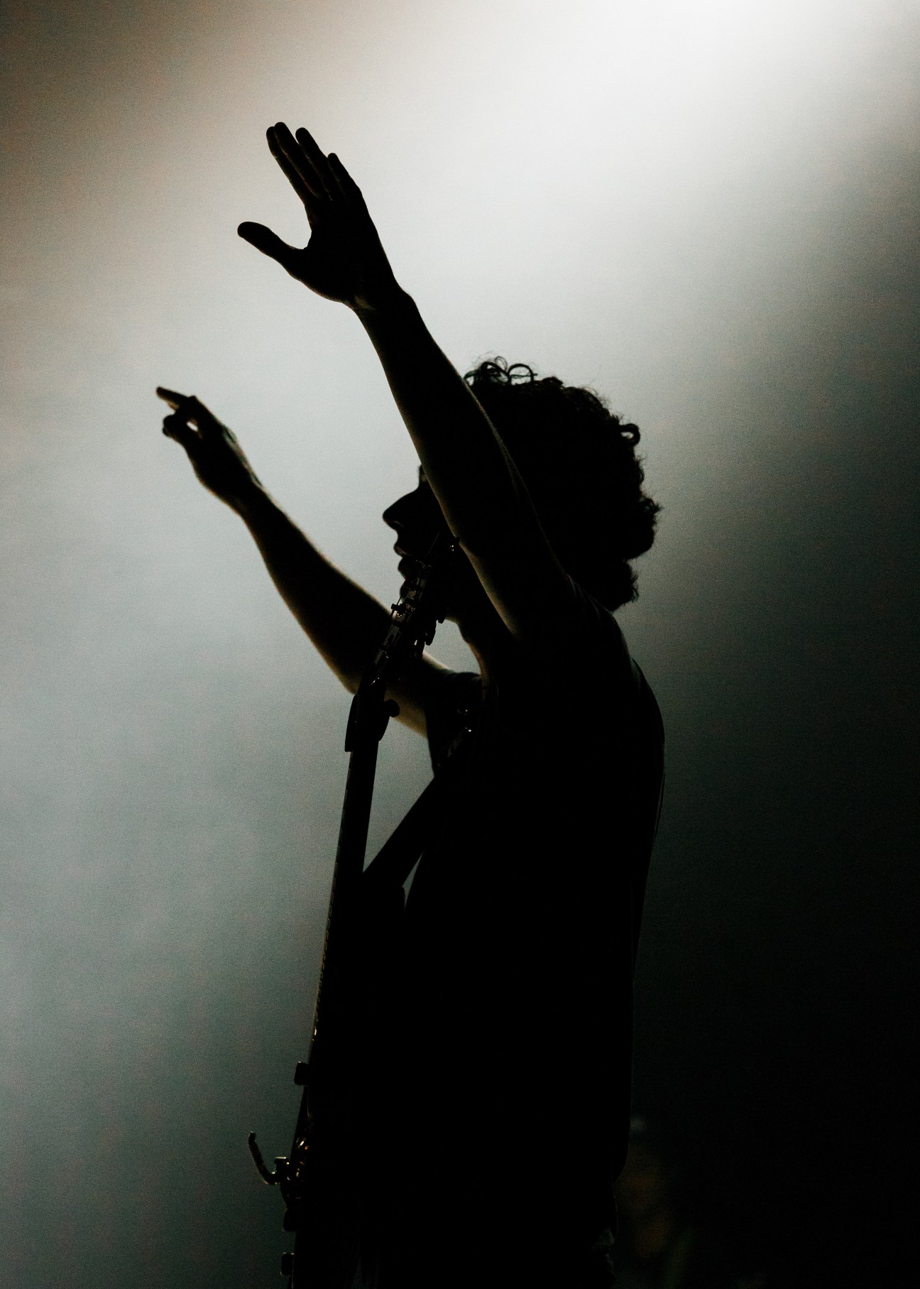 Silhouette of a musician performing at the Outcry Festival with raised arm holding microphone.