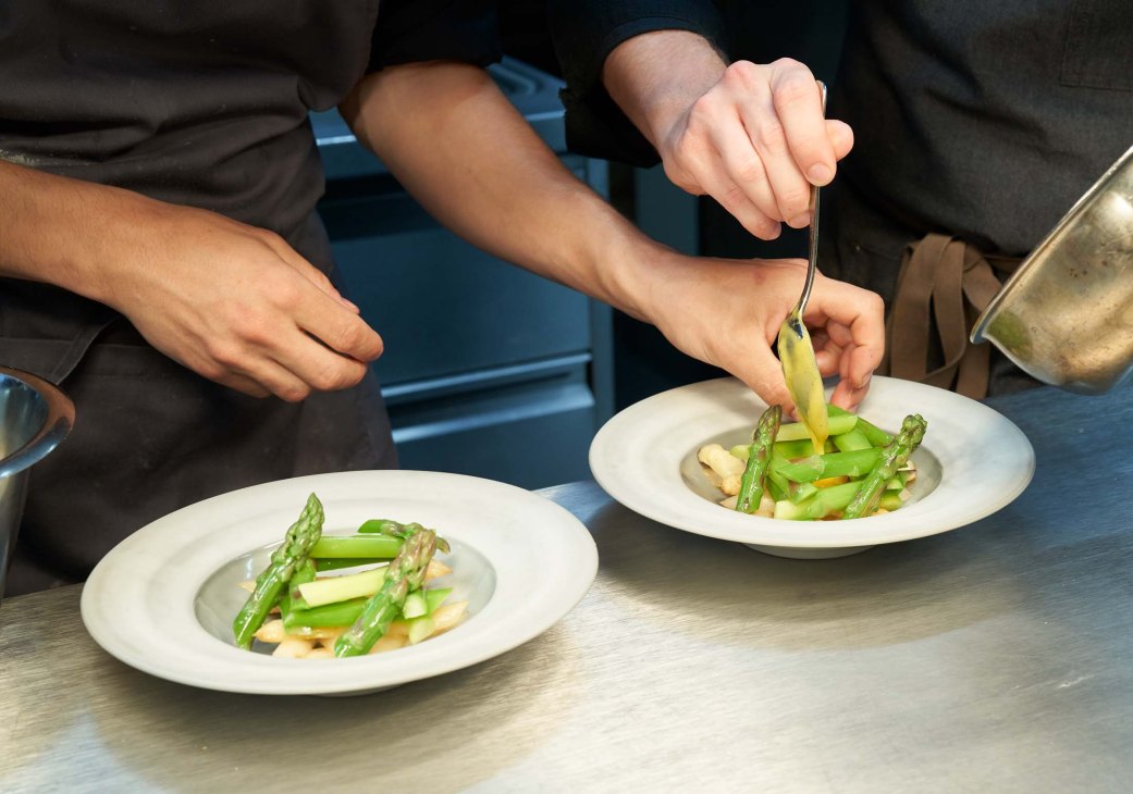 Chef's hands garnishing plated asparagus dishes with precision in a professional kitchen