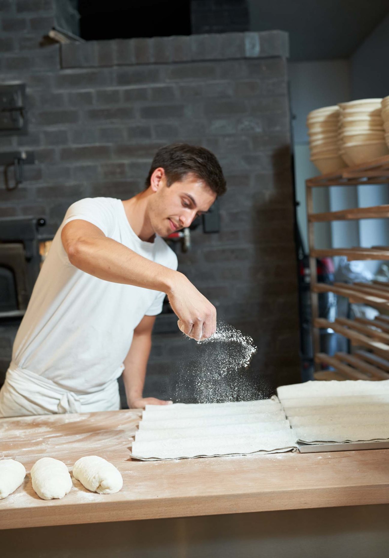 A baker dusting flour onto dough at a wooden work table in a traditional bakery
