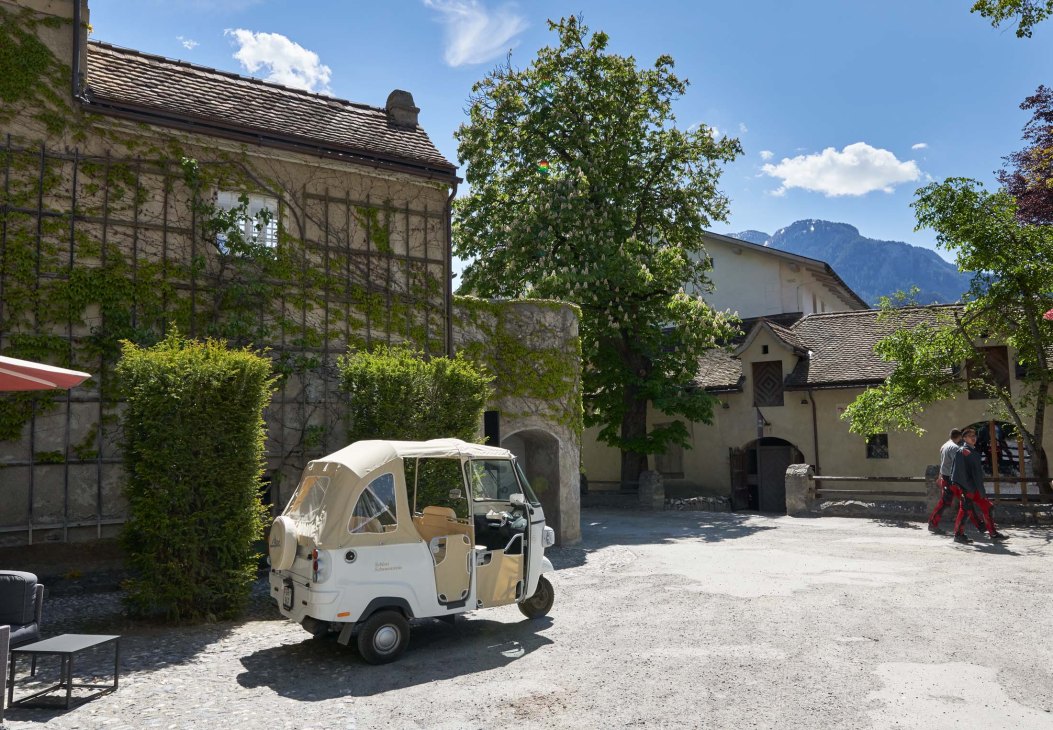 Stone castle buildings with ivy-covered walls and a white three-wheeled vehicle parked in the courtyard