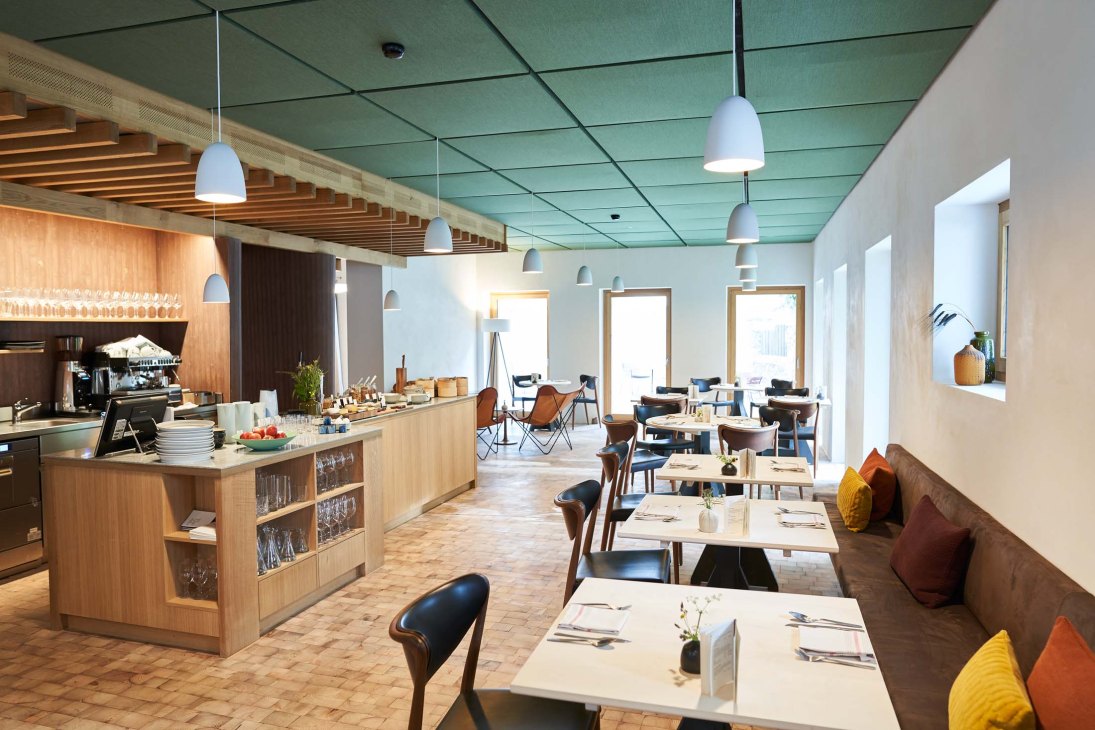 Modern dining room with wooden bar, white pendant lights, and tables set for service at Casa Caminada.