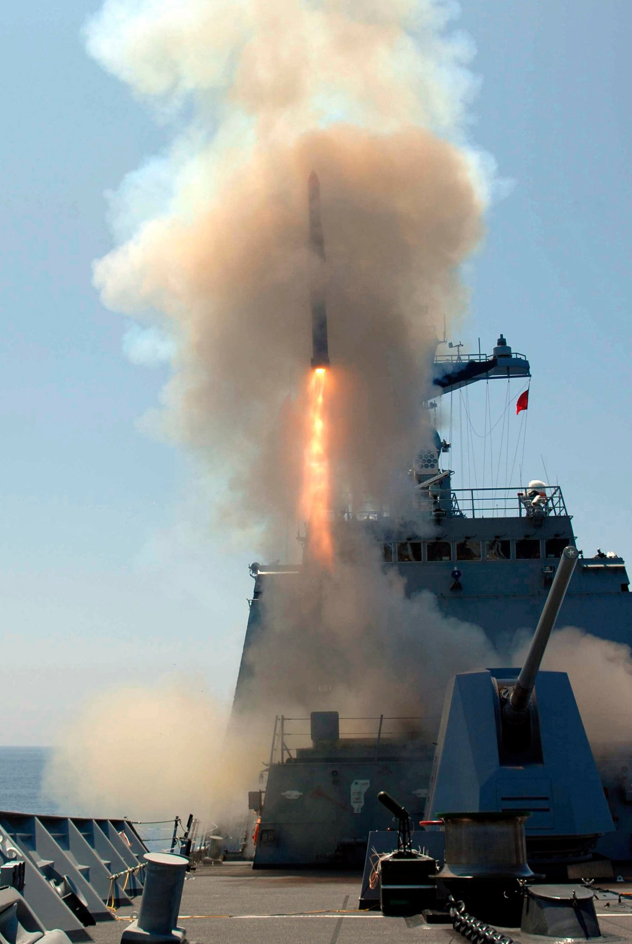 A naval vessel fires a cruise missile into the sky amid smoke and flame.