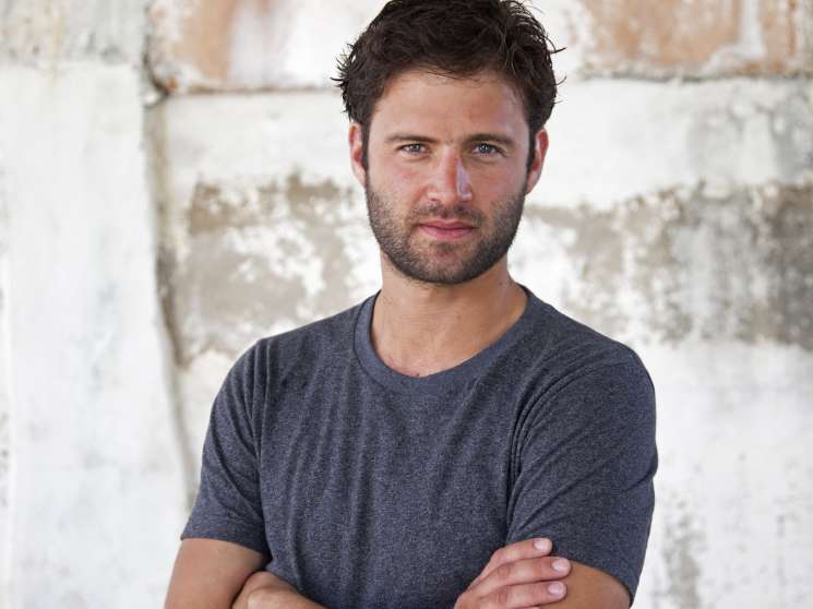 War photographer Sebastian Meyer poses with arms crossed against a weathered whitewashed brick wall.