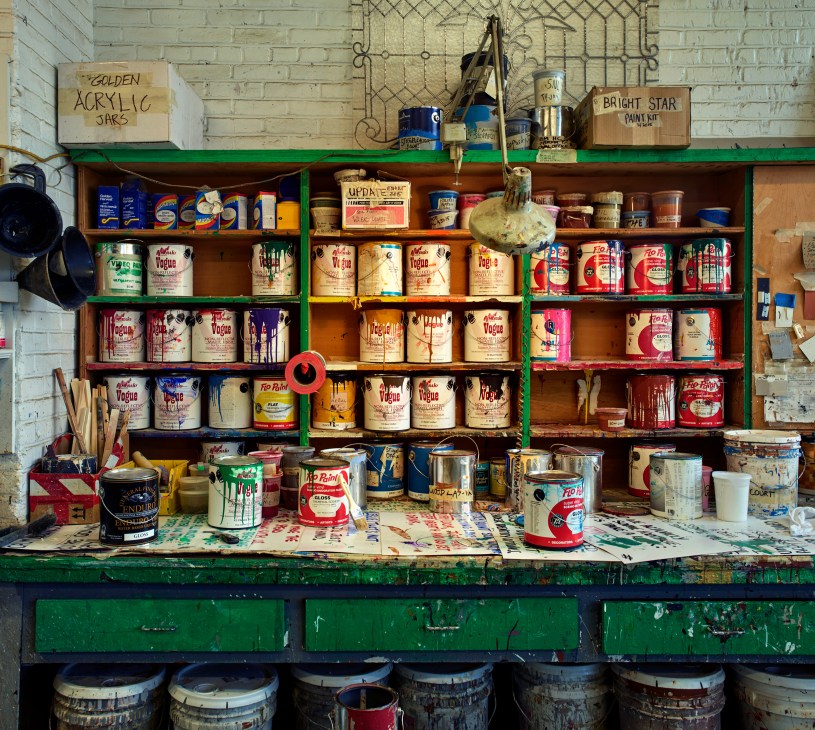 Shelves stocked with paint cans, brushes, and supplies at Stiegelbauer Associates' scenic shop.