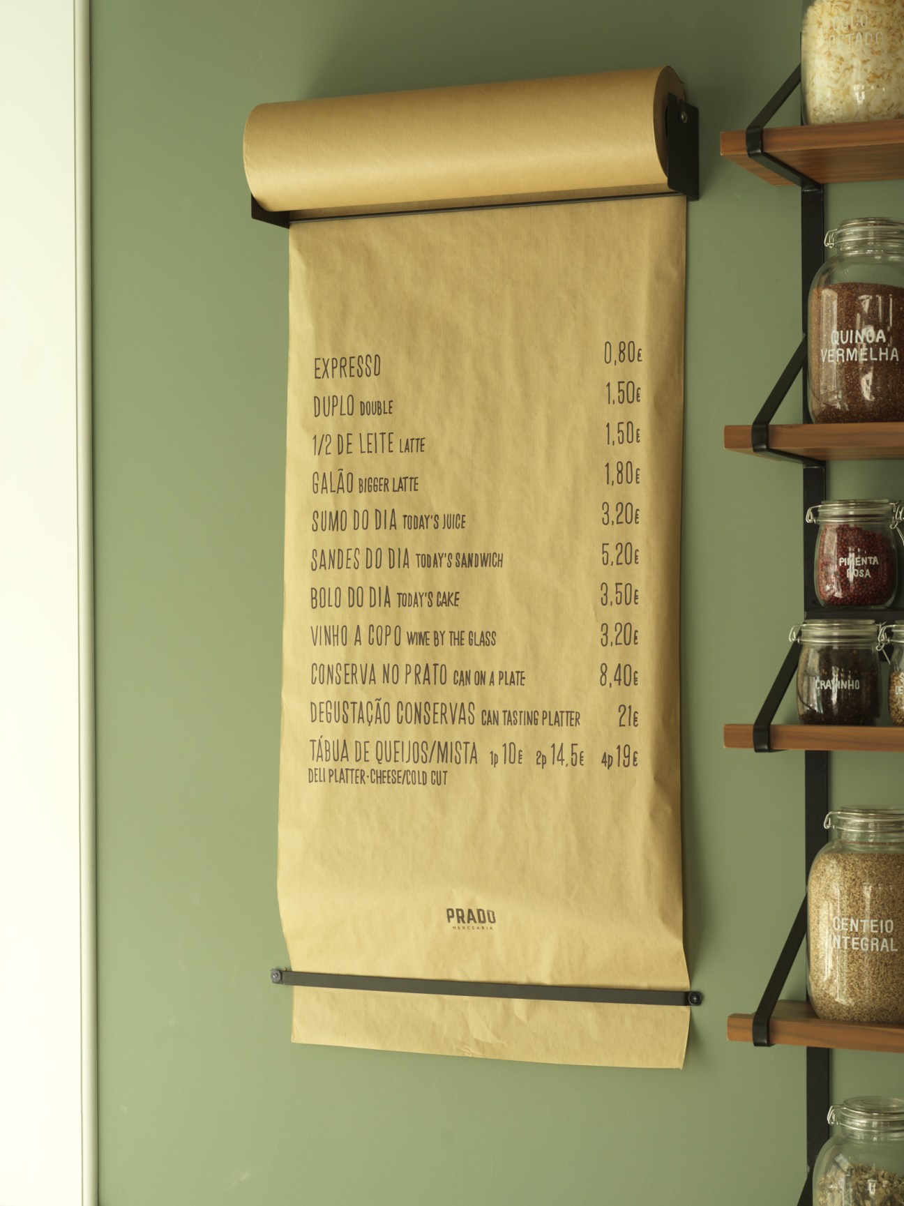 Prado Mercearia's lunch menu printed on kraft paper with a brass holder against sage green wall.