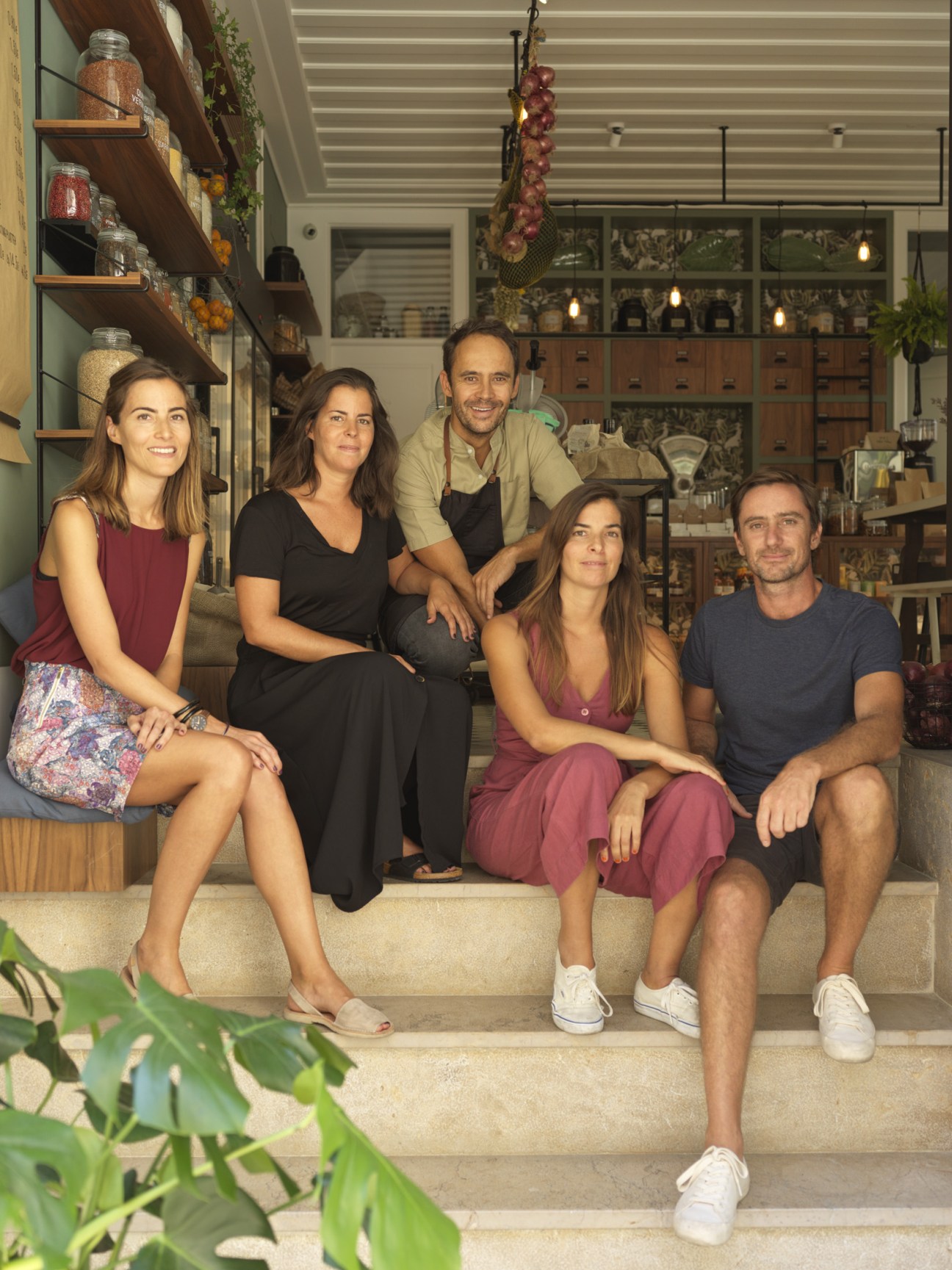 Five people sitting on steps outside Prado Mercearia grocery store in Lisbon.