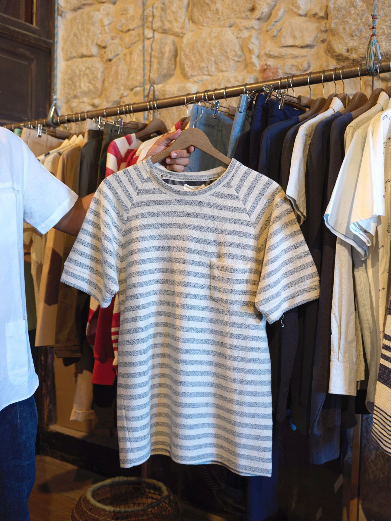 Striped t-shirt on wooden hanger displayed in La Paz store with stone wall background and other clothing.